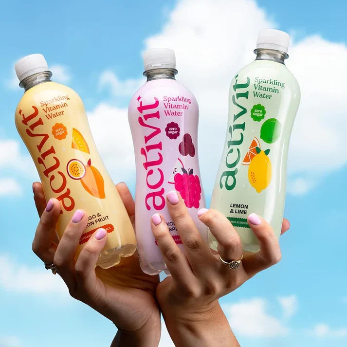 Hands holding Activit Mango & Passion Fruit, Blackcurrant & Raspberry and Lemon & Lime bottles against a blue sky